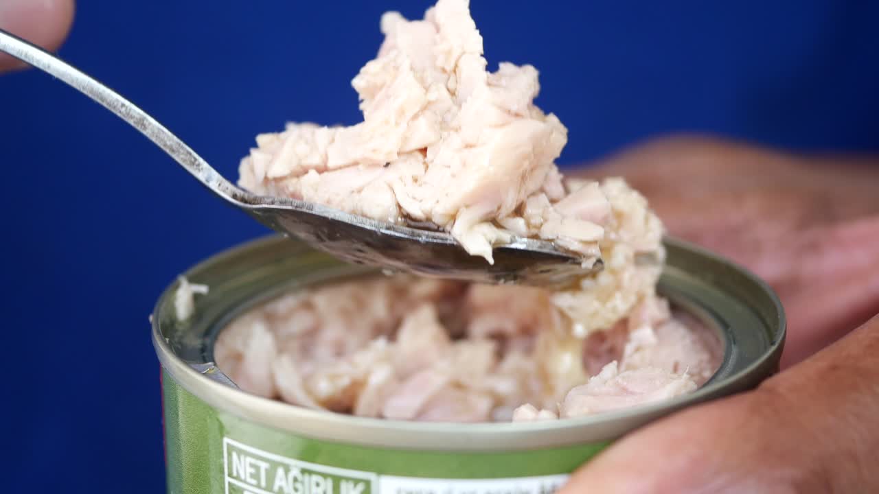 Hands open a can of tuna with a spoon