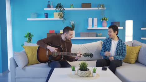 the older brother playing the guitar is singing with his younger brother at home.