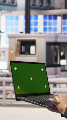 vertical video technician in industrial plant using green screen laptop to diagnose equipment