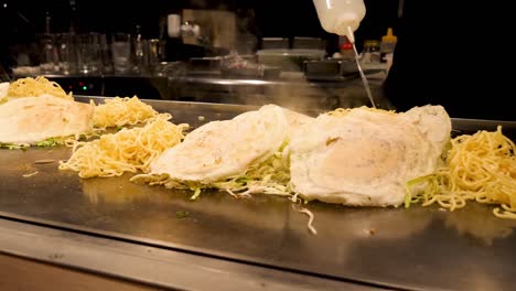 A-Japanese-chef-cooks-a-traditional-Okonomiyaki-savory-pancake-on-a-tepanyaki-grill-in-Kyoto,-Japan