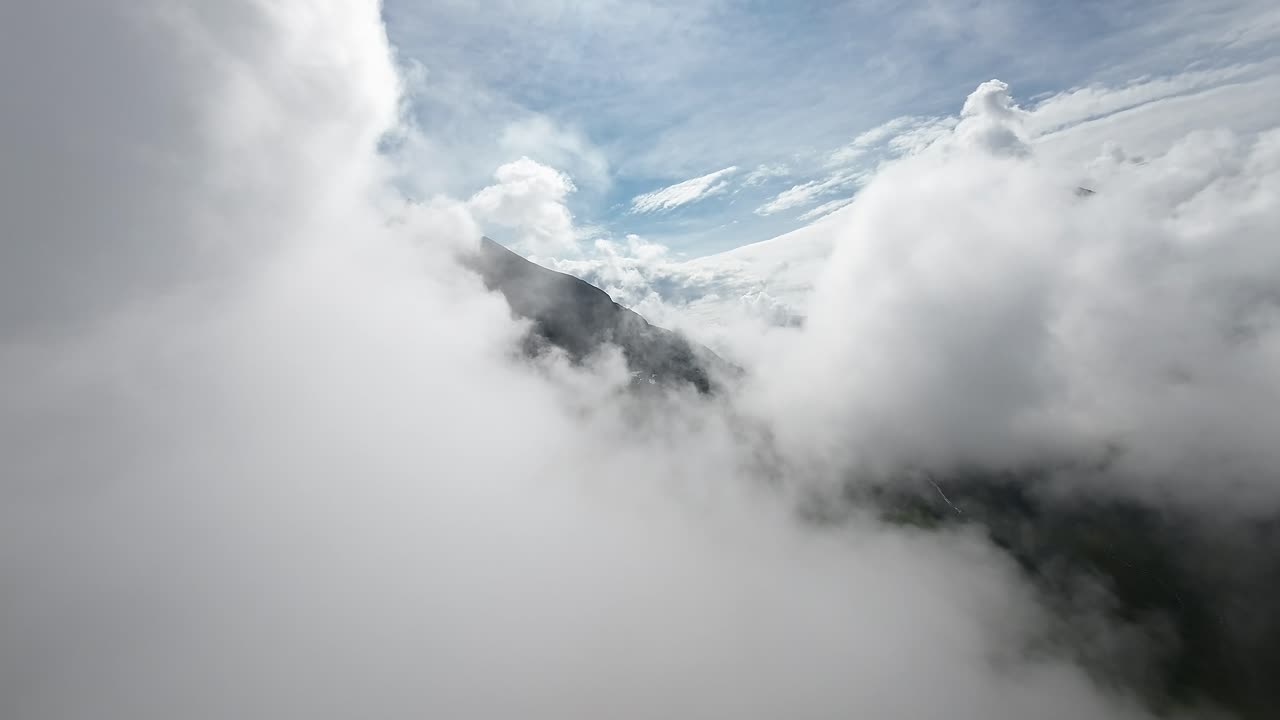 FPV drone soars amidst billowing clouds, unveiling a majestic mountain's grandeur, capturing nature's breathtaking spectacle from above
