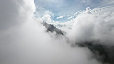 FPV-drone-soars-amidst-billowing-clouds,-unveiling-a-majestic-mountain's-grandeur,-capturing-nature's-breathtaking-spectacle-from-above