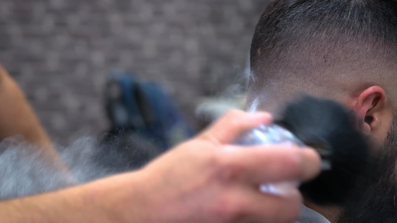 un barbero empolva la nuca de un cliente después de un corte de pelo