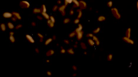 muchos cacahuetes iluminados cayendo hacia la lente y cayendo sobre la superficie negra
