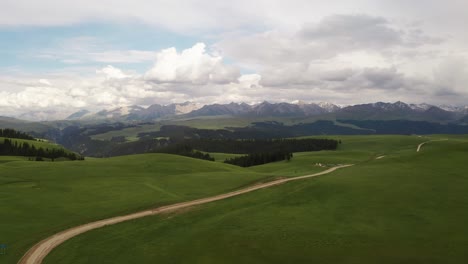 mountain peaks and grassland are under white clouds.