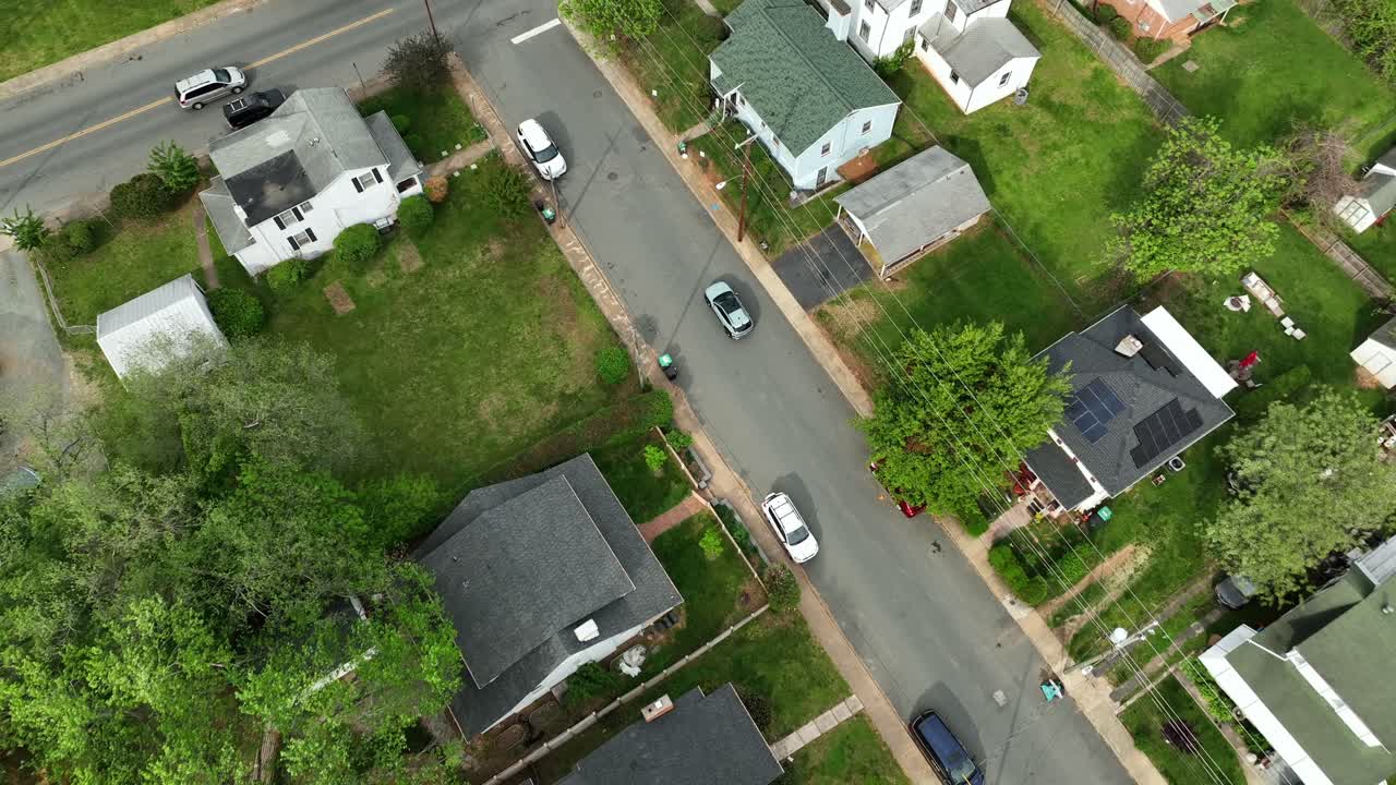 Car on street of american neighborhood during sunny day in spring season. Colorful roofs of houses in quiet housing area of US. Aerial top down flyover. Solar panels on top of home.