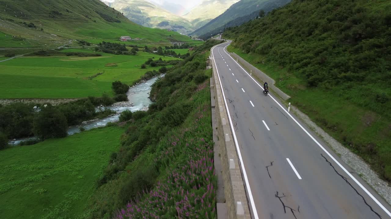 스위스 알프스 산맥의 도로에서 자전거를 타고 있는 관광객들과 무인기에서 찍은 하늘의 무지개