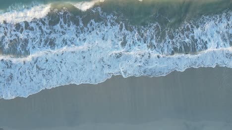 UAE:-Aerial-view-of-waves-breaks-on-the-beach,-Bird's-eye-view-of-ocean-waves-crashing-and-foaming-against-the-empty-shore,-rough-sea-view