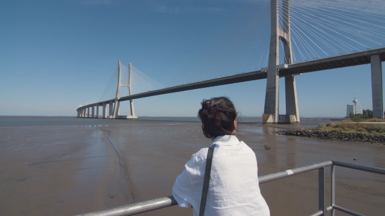 Young woman enjoys the view of the river and bridge. Low tide. Vasco da Gama bridge in Tagus river. Contemplation in solitude. Architectural wonder