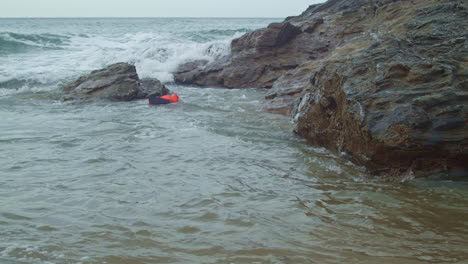 Schwimmweste-Schwimmt-Entlang-Strandfelsen,-Während-Die-Wellen-Am-Ufer-Krachen