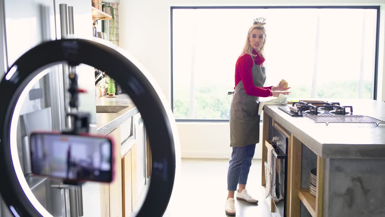 Prompted by smartphone woman adjusting framing with LED ring, wiping island prepping cooking area
