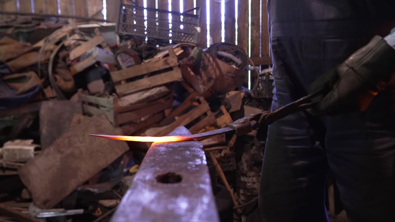 Blacksmith working on hot metal on an anvil in a cluttered workshop