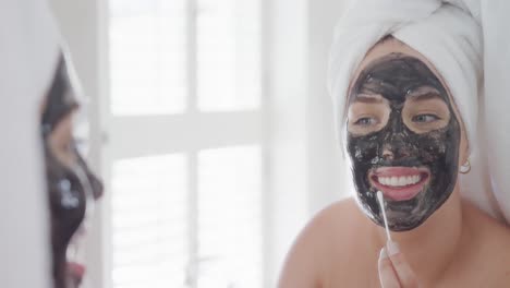 mujer caucásica feliz de talla grande con una toalla en la cabeza haciendo una máscara en cámara lenta