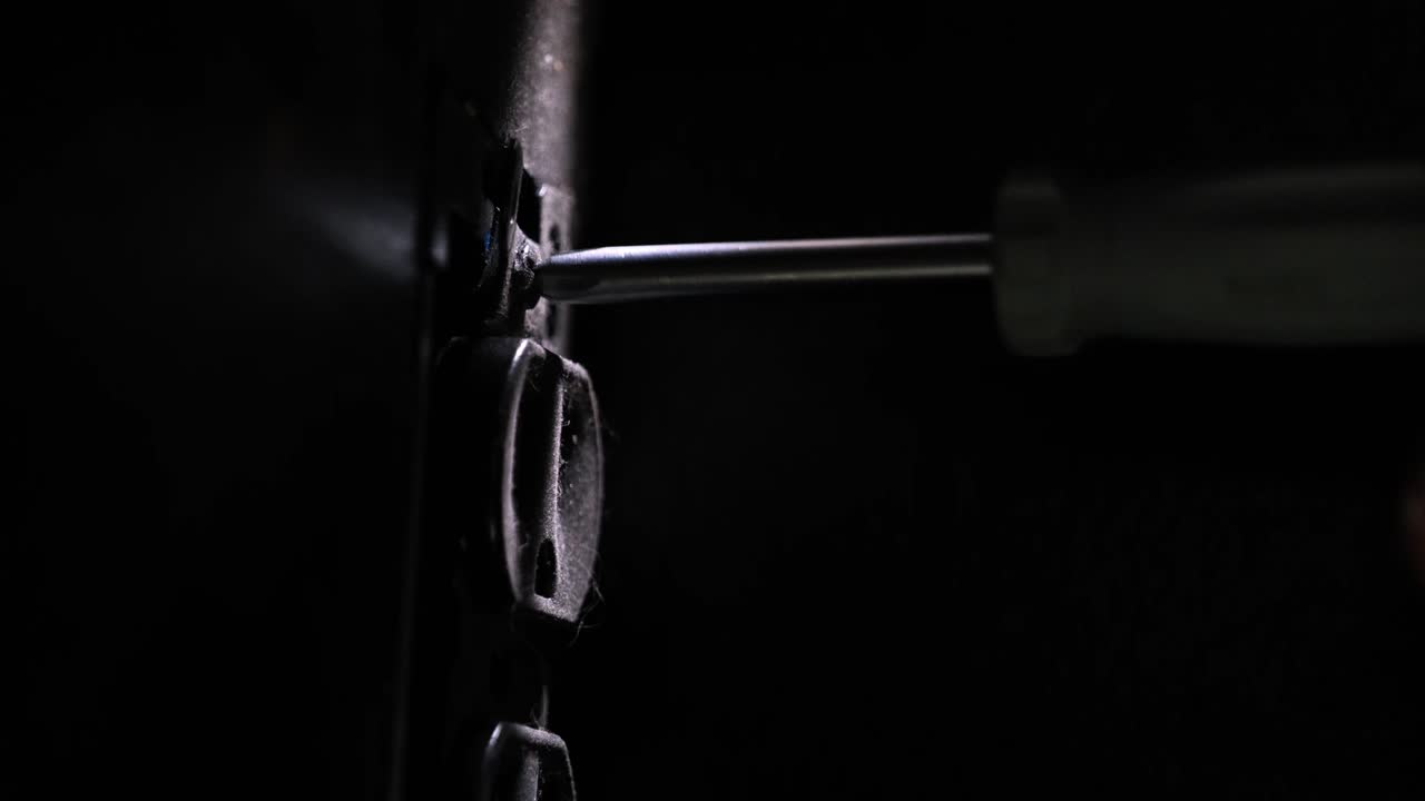 atornillar el tornillo de enchufe de 3 clavijas estadounidense con un destornillador de cabeza phillips en una iluminación oscura dramática - en el cine 4k