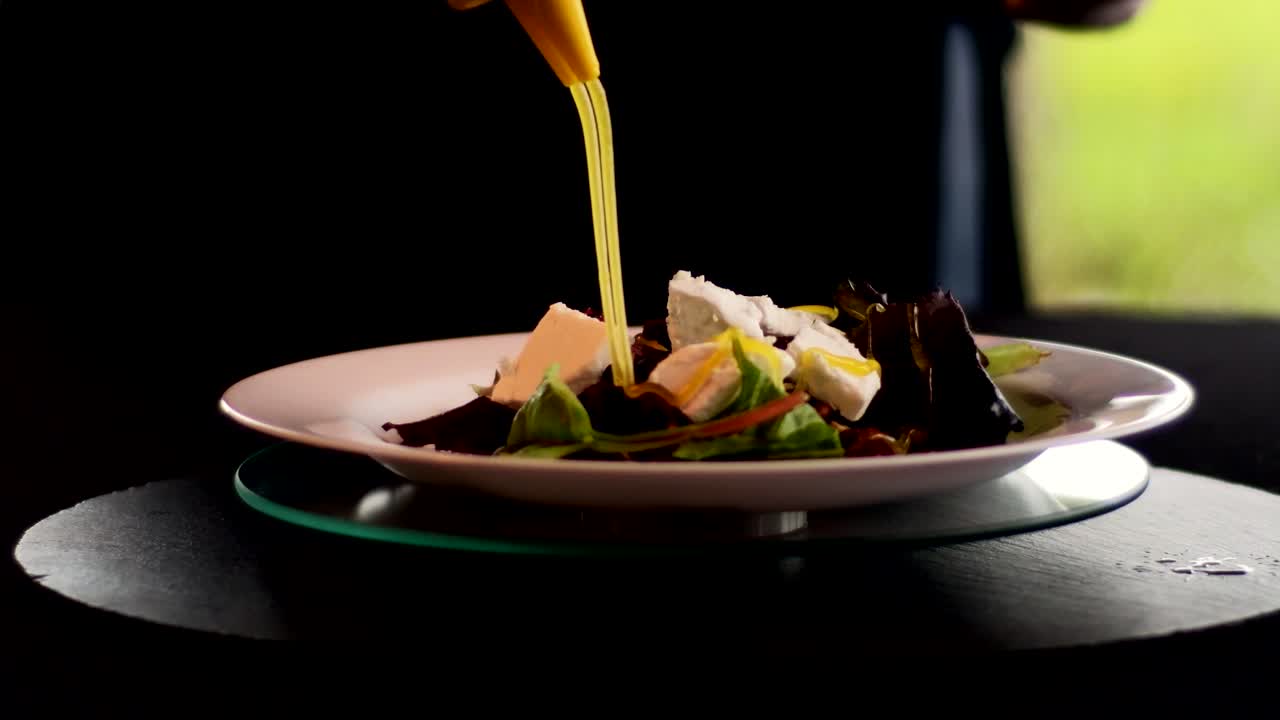 manos poniendo un aderezo en una ensalada chef