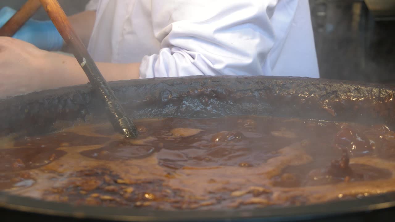 Uno chef in uniforme bianca mescola uno stufato di miso marrone bollente usando un mestolo grande.