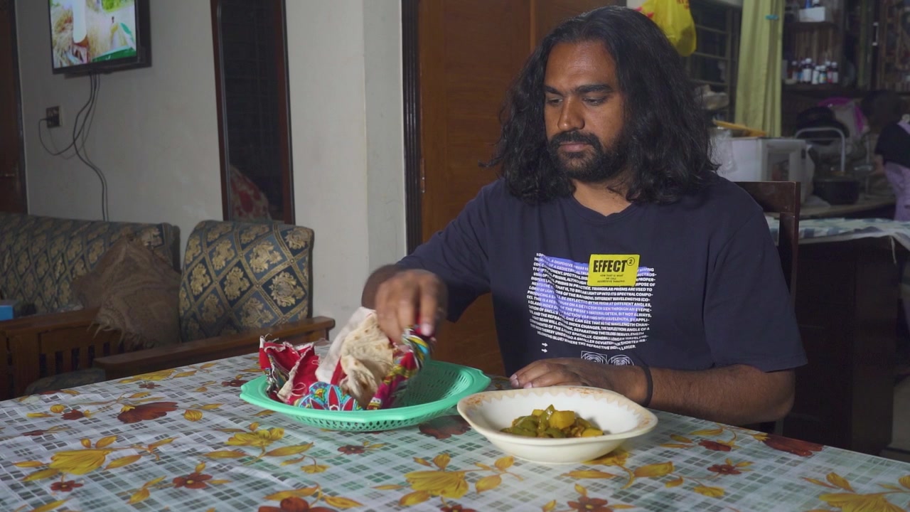 Un uomo asiatico con i capelli lunghi inizia a gustare il suo cibo tradizionale pakistano seduto al tavolo da pranzo in casa, Islamabad Pakistan