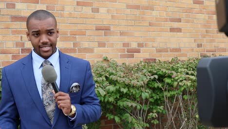 Moving-Shot-Behind-Camera-Revealing-Young-African-American-Male-News-Reporter-Making-a-Live-Report