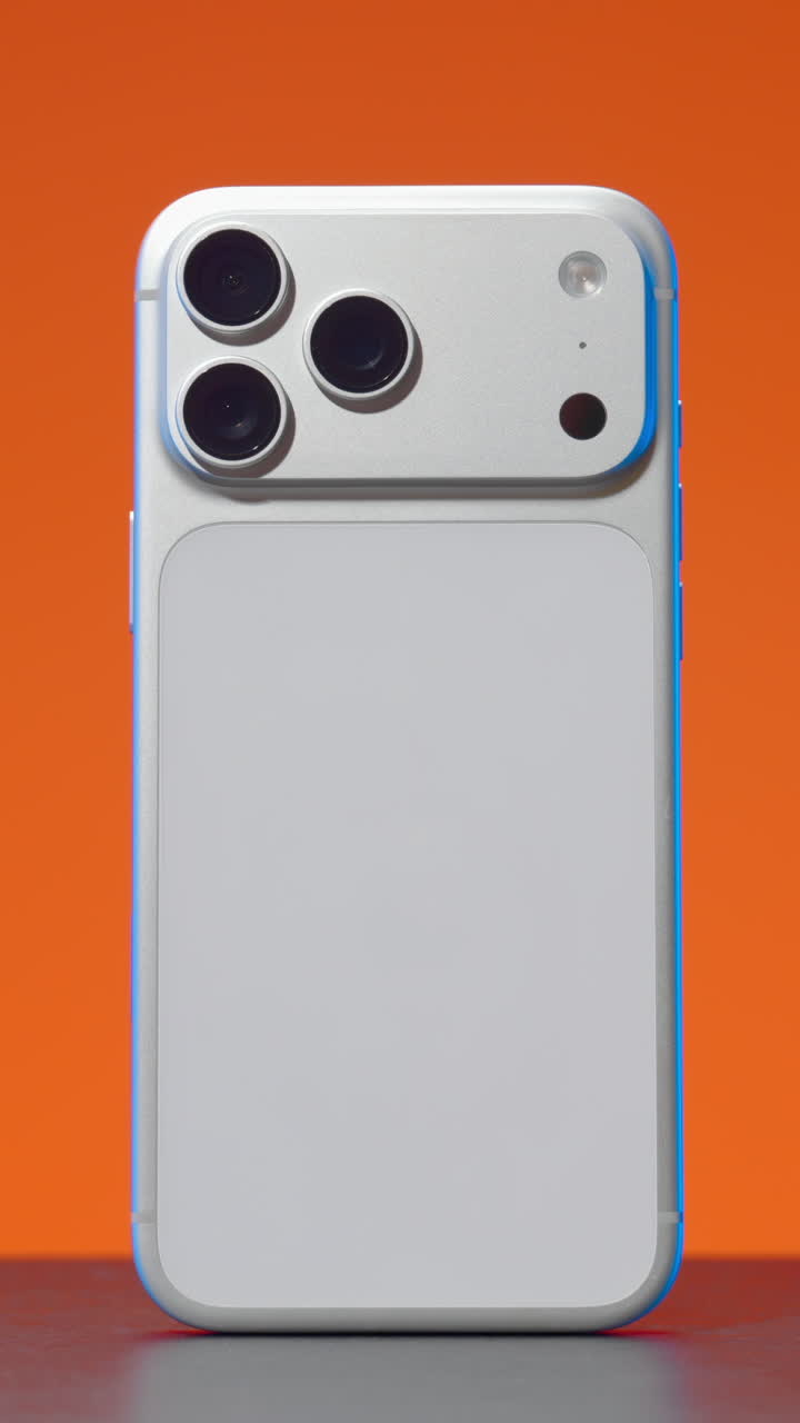 Futuristic silver mobile phone with a new camera design rotating against an orange background. Action