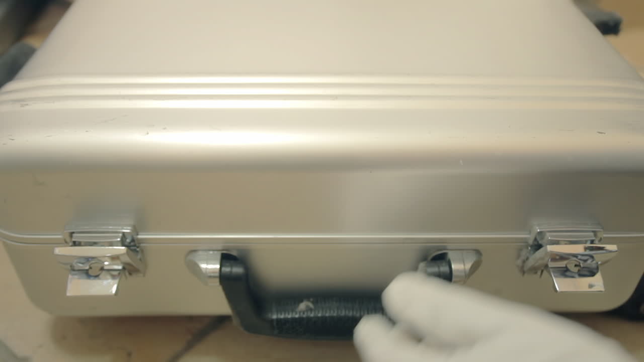 ⁇  장갑을 입은 살인자의 손이 금속 컨테이너 케이스를 열고 총을 들고 조심스럽게 닫습니다.