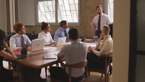 Middle-aged-businessman-talks-at-meeting,-seen-from-doorway