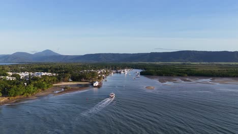 drone footage captures boats navigating a tropical marina with lush greenery and distant mountains under clear skies