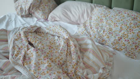 unmade bed with floral and striped bedding