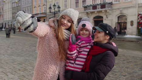 Lesbian-couple-tourists-with-adoption-child-girl-taking-selfie-or-making-video-chat-on-city-street