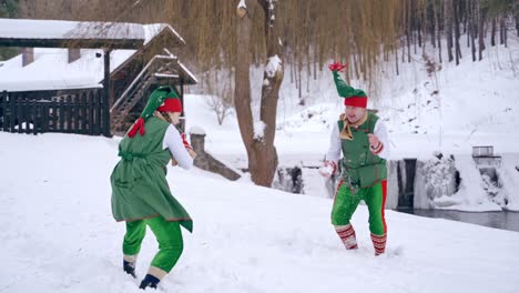 funny elves play snowballs in nature. snowy background and two joyful fairy characters in green costumes having time together outdoors. christmas.