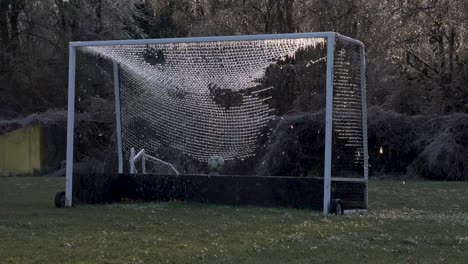 slow motion: a soccer ball slams an icy net of a soccer goal exploding shattered ice into the air