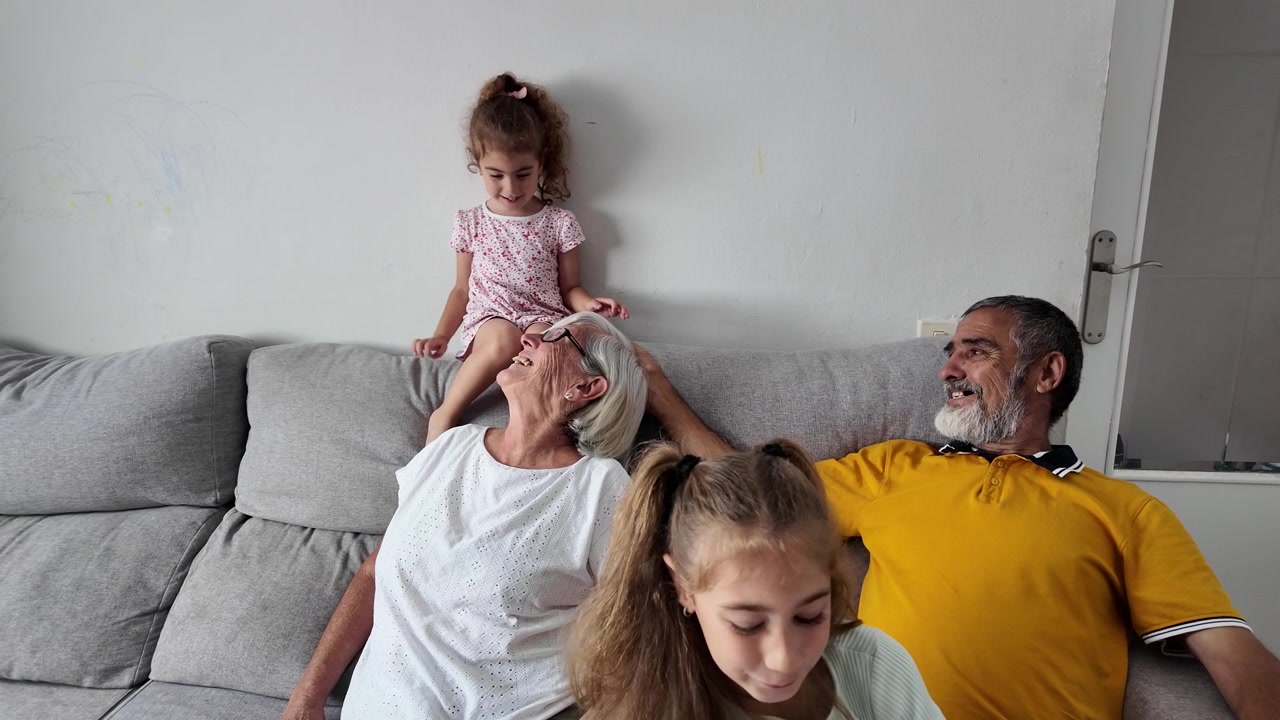 Abuelos felices jugando con sus nietas en el sofá de casa.