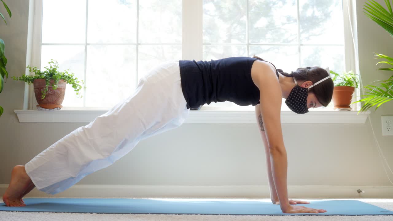 Graceful female yogi performing yoga stretches in her home while wearing a medical mask
