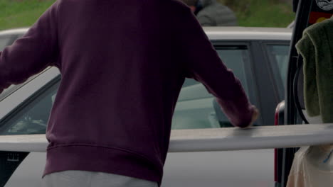 person cleaning surfboard inside vehicle trunk, preparation before sport