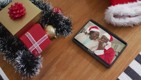 smiling senior african american couple wearing santa hats on christmas video call on tablet