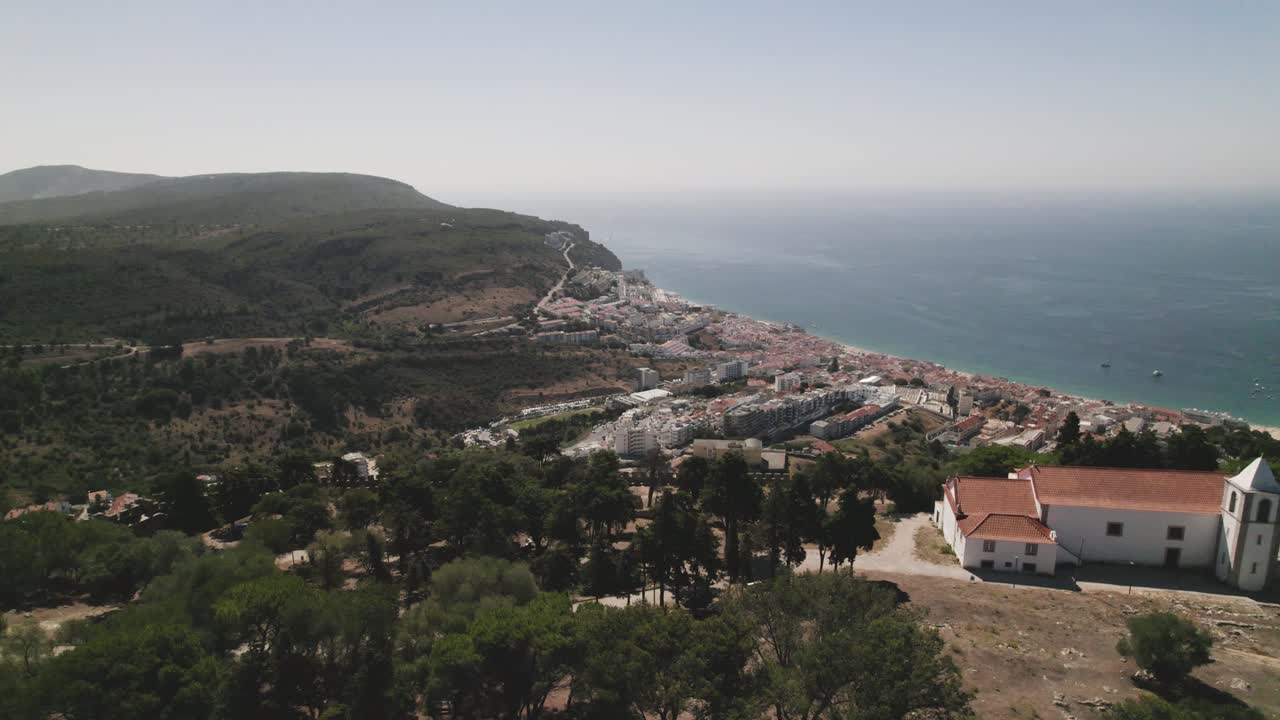 vuelo aéreo a través del castillo en la cima de la colina revelando la pintoresca costa de sesimbra en portugal