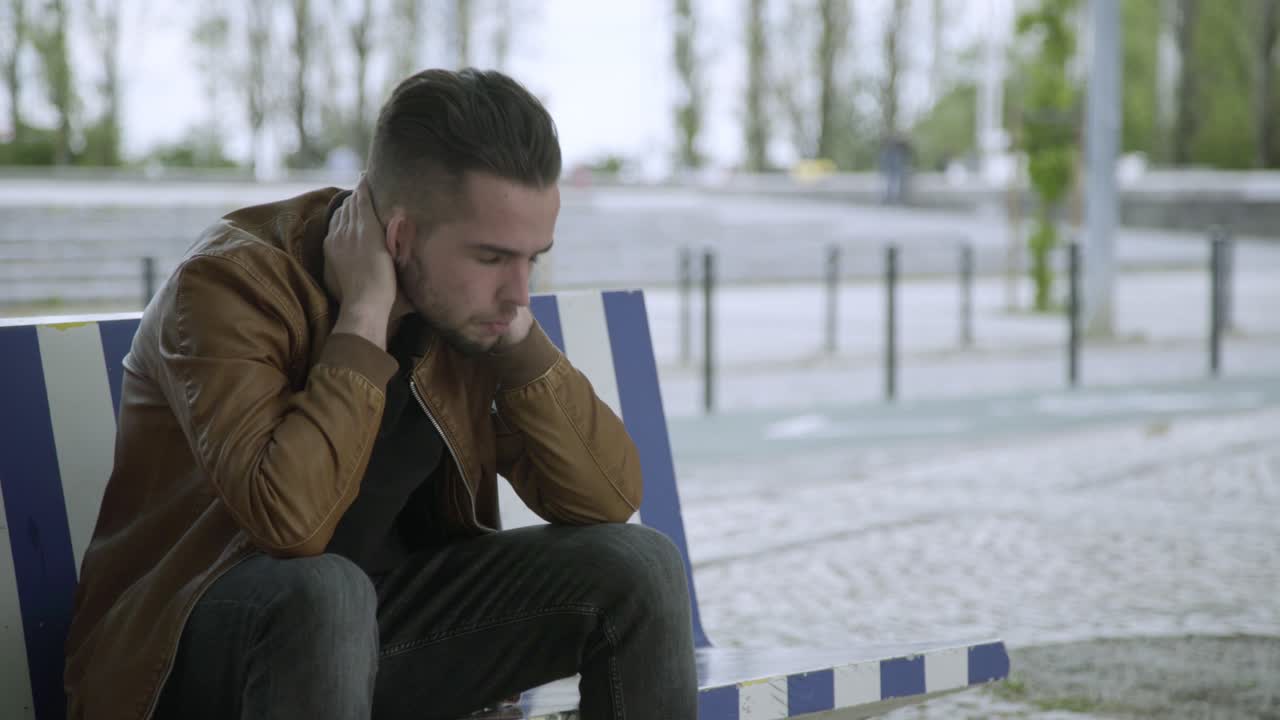 un joven enojado frotando la cara afuera.