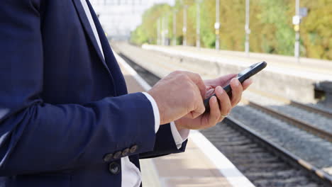 primer plano de un hombre de negocios de pie en una plataforma ferroviaria usando un teléfono móvil