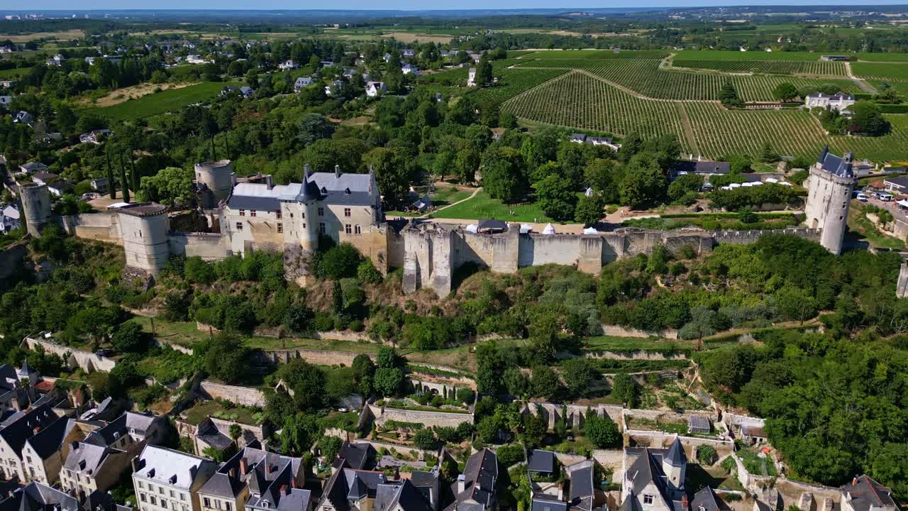 Drönare etablerar Fortresse Royale de Chinon-slottkomplex omgivet av stad och träd, panoramisk flygbild mitt på dagen