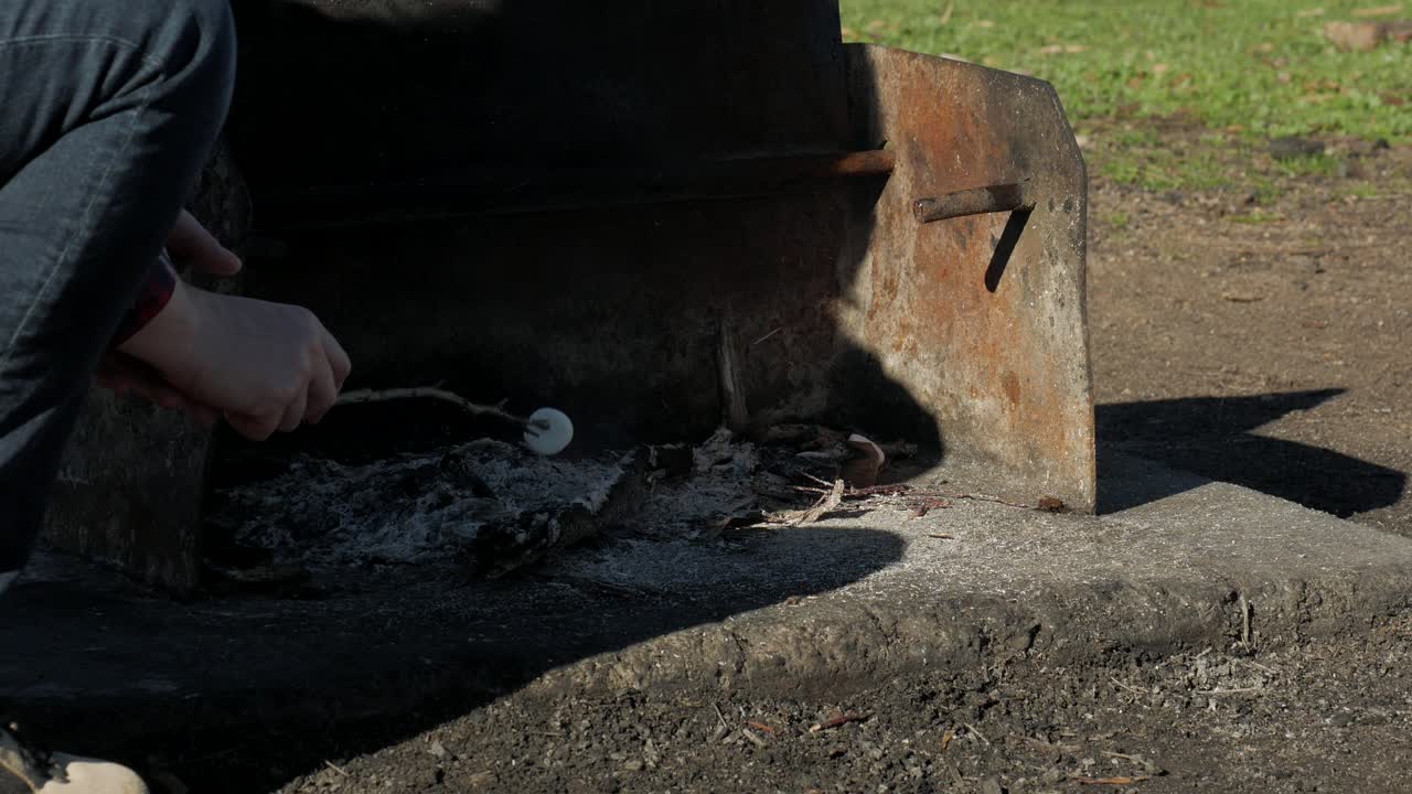 mujer cocina malvavisco en un palo, al aire libre sobre brasas abiertas