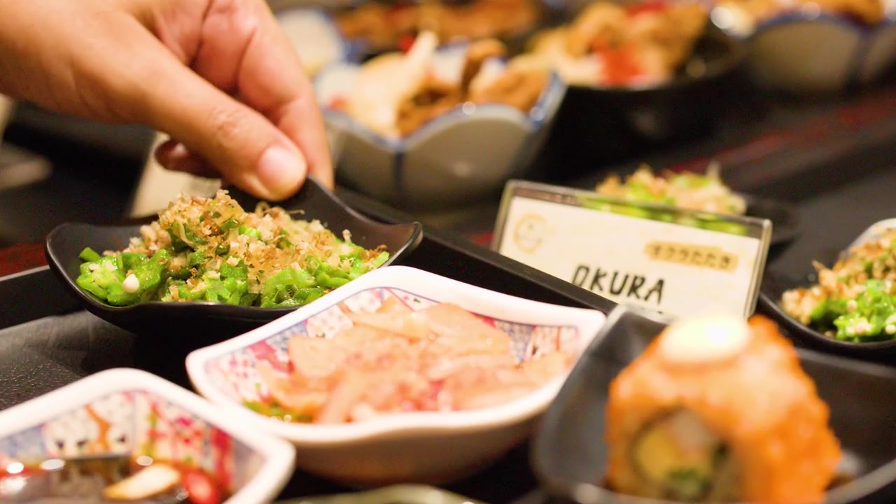 En person vælger små tallerkener med okra og burrerod fra en restaurantbuffet i Bangkok