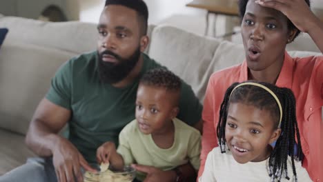 excited african american parents with son and daughter watching sport on tv at home, slow motion