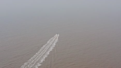 Aerial-drone-shot-towards-a-speed-boat-on-muddy-water-hazy-day