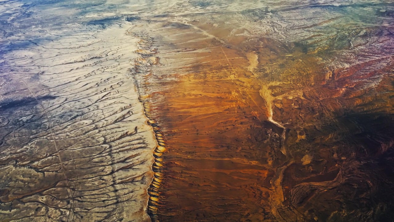 Dramatic canyon system and deeply incised erosion channels across desert landscape, aerial showcasing contrast of snow and dry red terrain