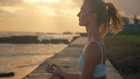 Mujer-En-Meditación-Zen-Sentada-En-Una-Alfombra-De-Yoga-Durante-La-Puesta-De-Sol-En-La-Costa,-Cámara-Lenta