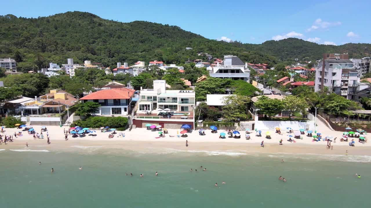 escena aérea de drones de lujosas casas y apartamentos frente al mar con mucha gente divirtiéndose en la playa en jurere internacional florianópolis