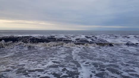 grey muddy foaming waves crash onto a black sandy beach