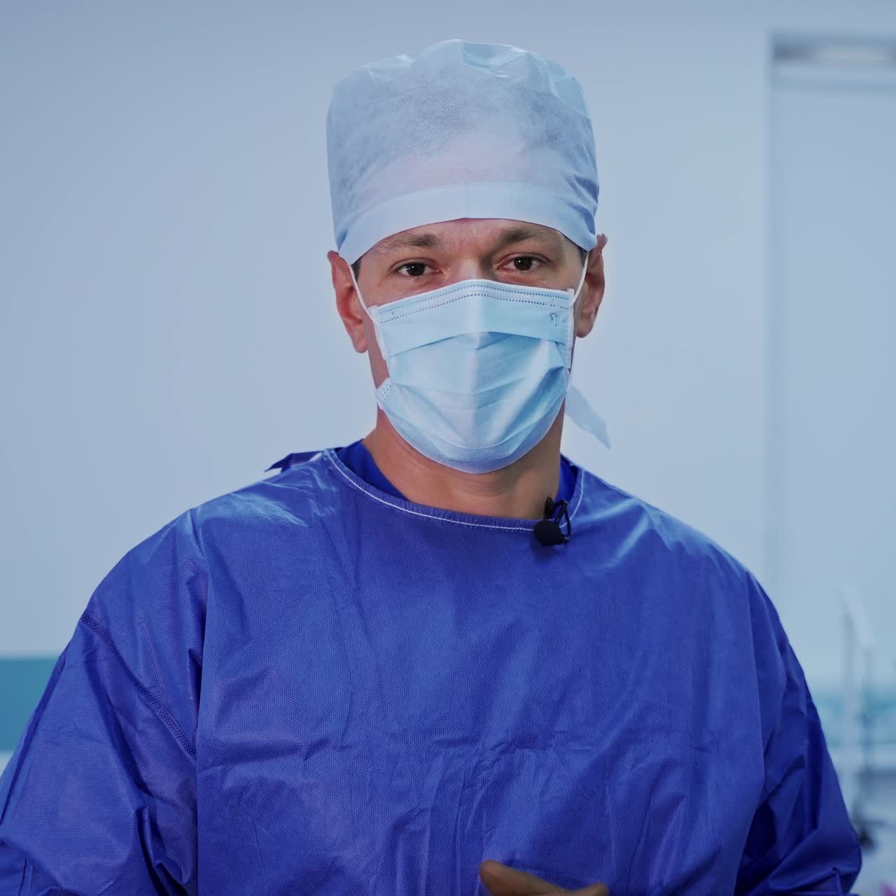 Portrait of a neurosurgeon. Professional doctor in blue medical uniform and mask looking to camera and talks in modern surgical room. Healthcare concept.