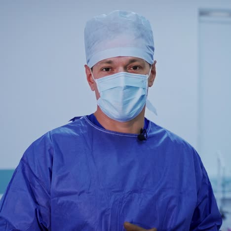 portrait of a neurosurgeon. professional doctor in blue medical uniform and mask looking to camera and talks in modern surgical room. healthcare concept.