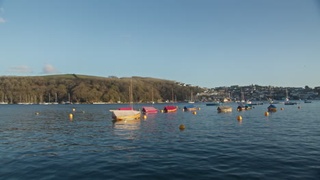 small sail boats docked in fowey harbour with scenic coast landscape of polruan in background- wide shot