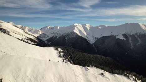 Sun-kissed-Fagaras-Mountains-under-blue-sky-with-snow-covered-peaks-and-pine-trees